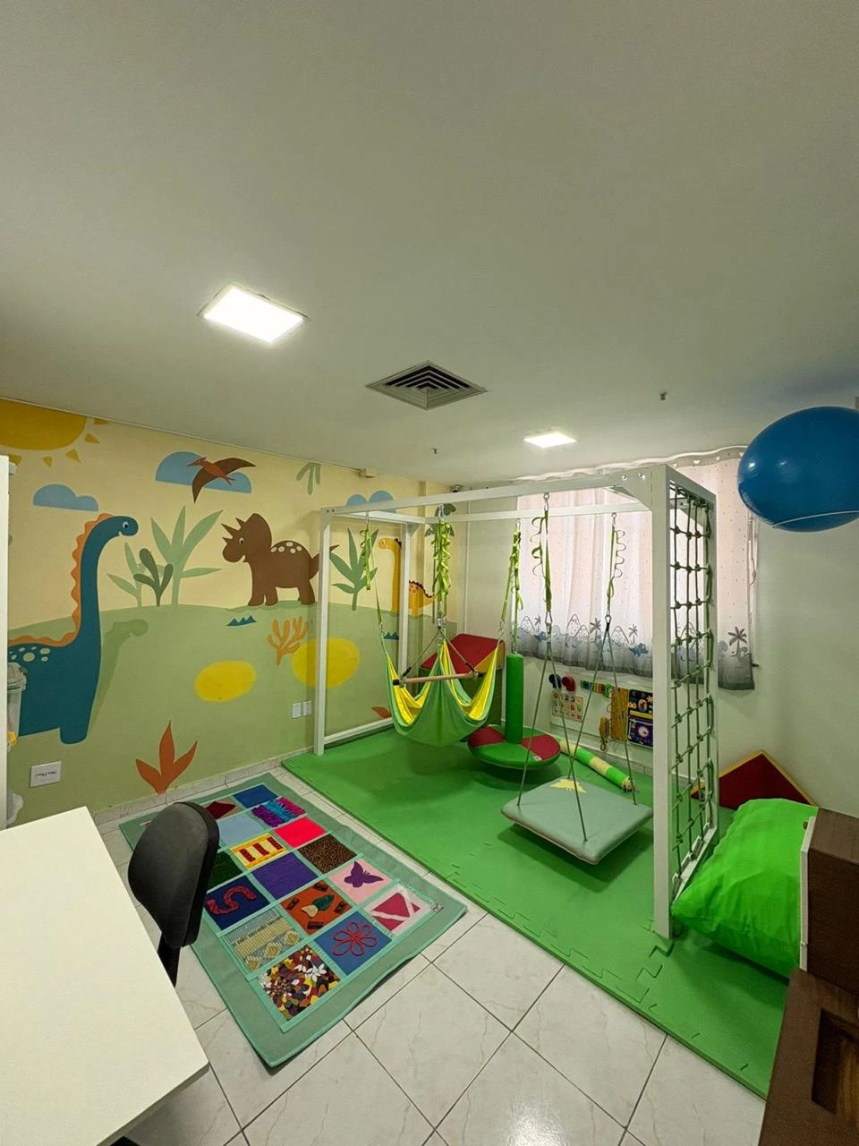 Sala de integração sensorial com balanços, tatame e mural de dinossauros