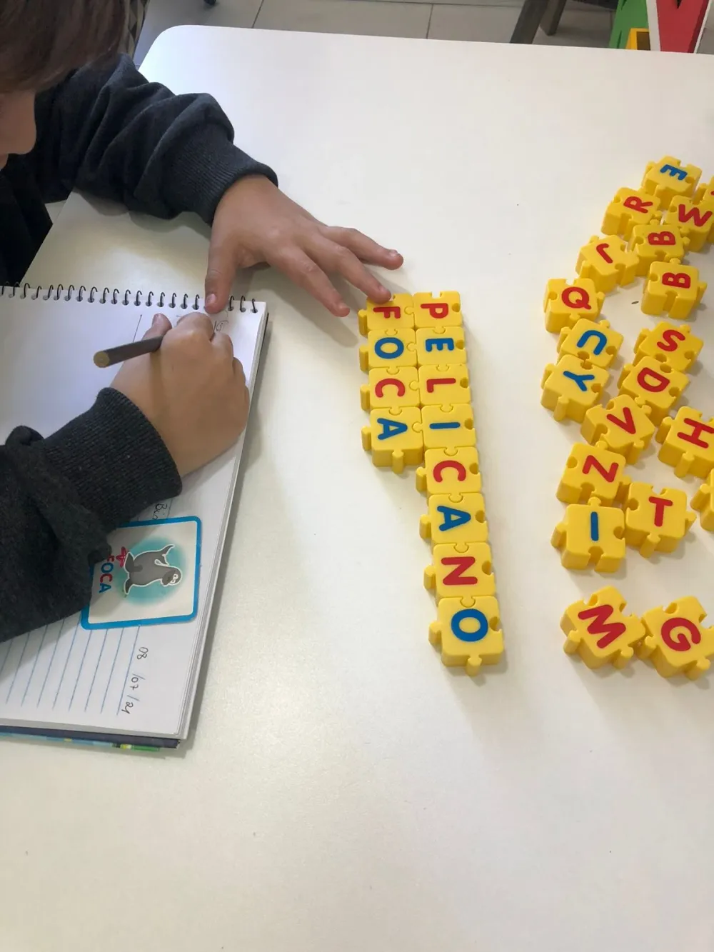 Criança formando palavras com alfabeto móvel e registrando no caderno